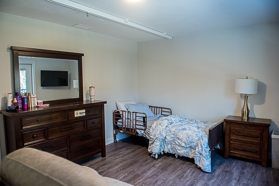 Picture of a bedroom with a large dresser & mirror, a side dresser at the end of the bed with a light