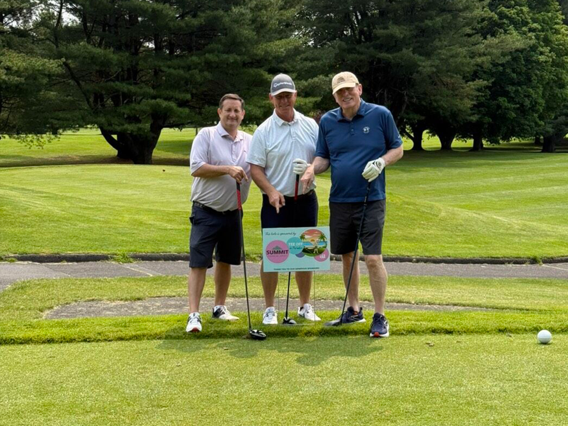 three men posing on the golf green in front of a hole sign